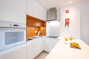 A compact kitchen with white cabinetry, a built-in oven, a microwave, a toaster, and a fruit display.