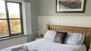 Una cama bien hecha con una colcha estampada de flores y dos almohadas, un cabecero de madera, una mesita de noche con una lámpara y un cuadro en la pared.
