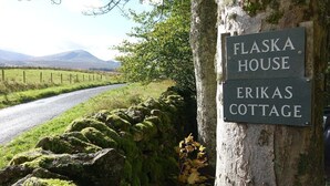Un letrero que indica 'Flaska House' y 'Erikas Cottage' en un árbol junto a una carretera rural.
