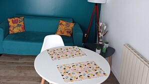 A teal-colored living room with a white sofa, two white chairs, a small round table with a lemon-patterned placemat, a floor lamp, and a radiator. - Cosy studio house (Le Havre)