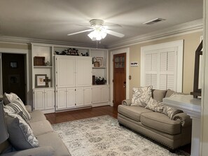 Un salon avec un canapé beige, un tapis à motifs, des meubles blancs et un ventilateur de plafond.