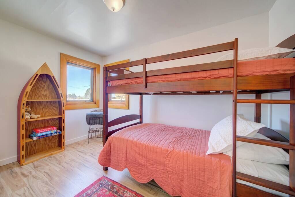 A bunk bed room with a wooden bookshelf, a desk, and a window.