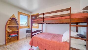 A bunk bed room with a wooden bookshelf, a desk, and a window.