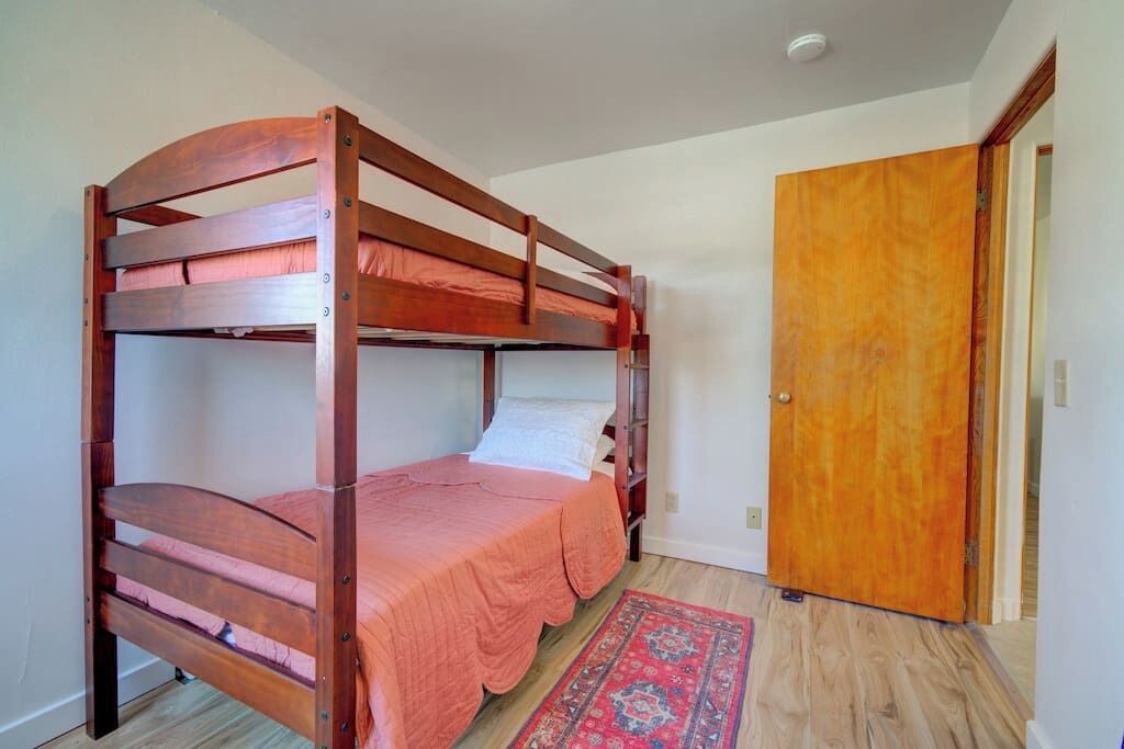 A bunk bed with a wooden frame and pink bedding in a room with a wooden door and a patterned rug.