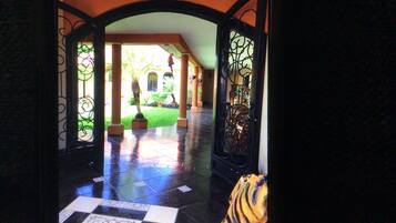 Vista a través de un ventanal de vidrio sobre un piso de baldosas que conduce a un patio con una palmera y un adorno colgante.