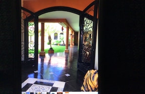 A view through a glass door with a tiled floor leading to a courtyard with a palm tree and a hanging ornament.