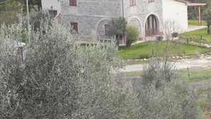 A stone building with a red-tiled roof, arched windows, and a small garden area. - Luxury Country House in Tuscany (Semproniano)