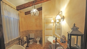 A bathroom with a bathtub, toilet, bidet, vanity, and a chandelier. - Luxury Country House in Tuscany (Semproniano)