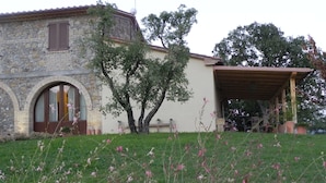 A stone building with a covered porch and a grassy area with pink flowers. - Luxury Country House in Tuscany (Semproniano)
