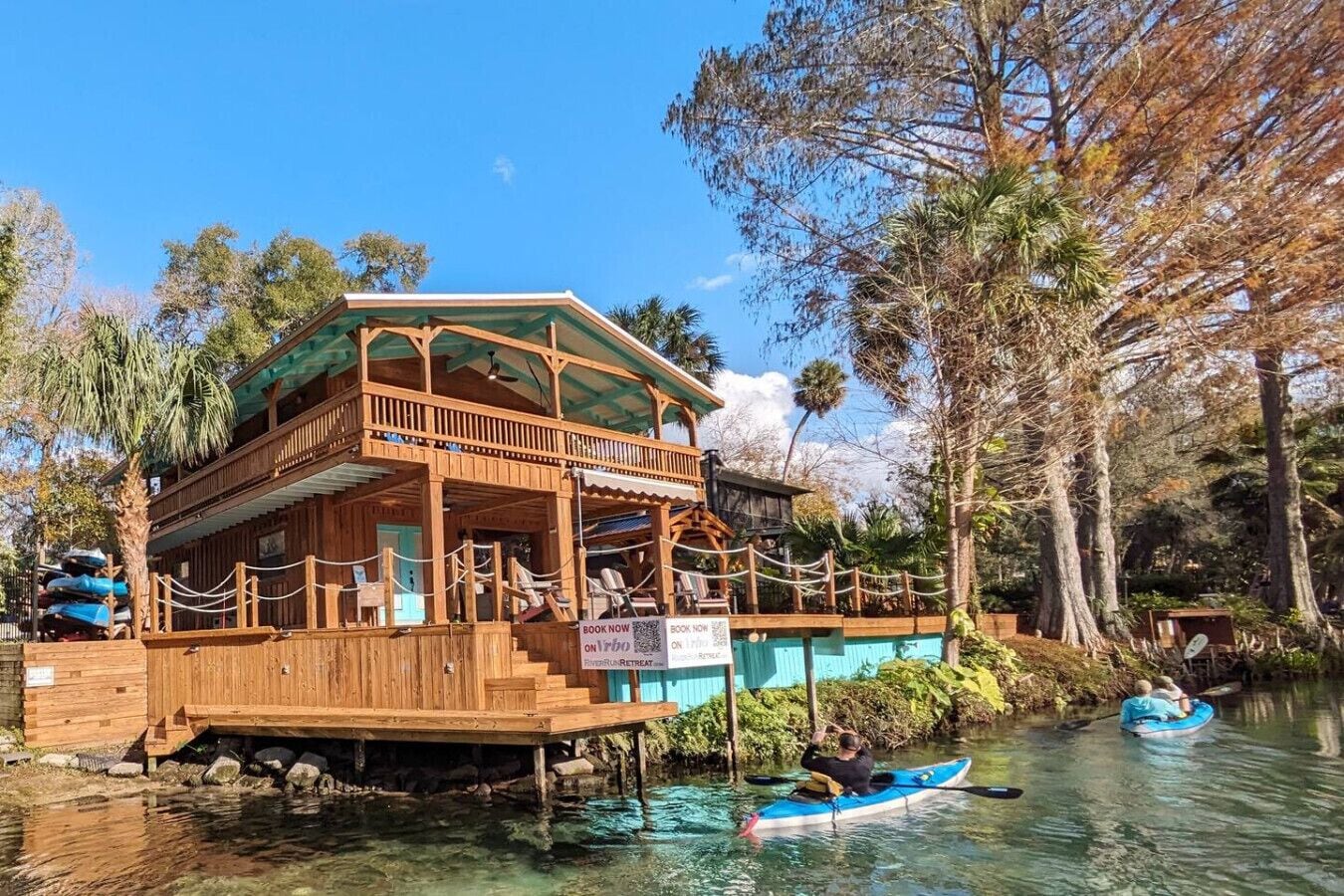 Eine Holzhütte mit Balkon, auf Stelzen über Wasser gebaut, umgeben von Bäumen.
