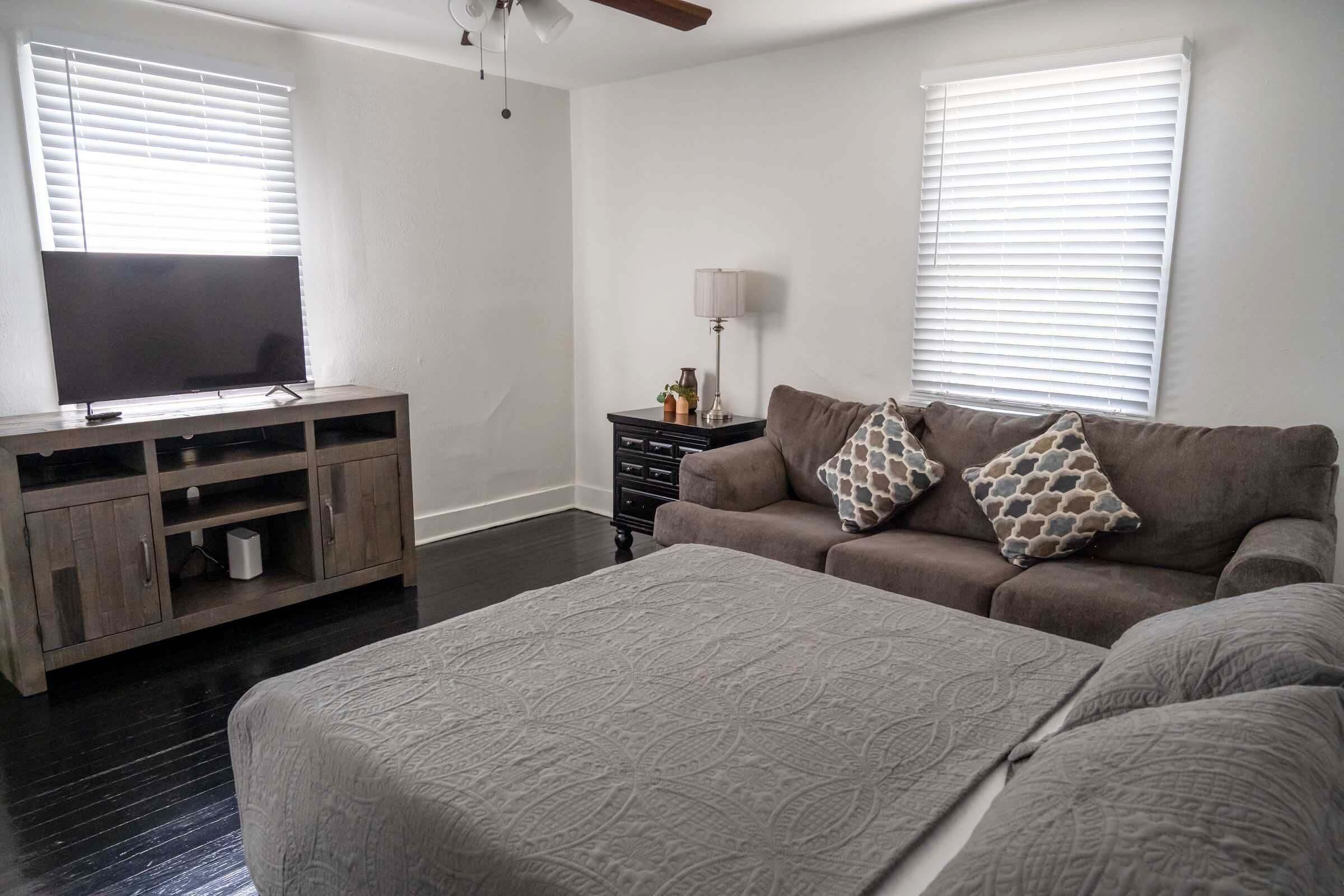 A bedroom with a large bed, a sofa, a TV on a wooden stand, and a lamp on a side table.