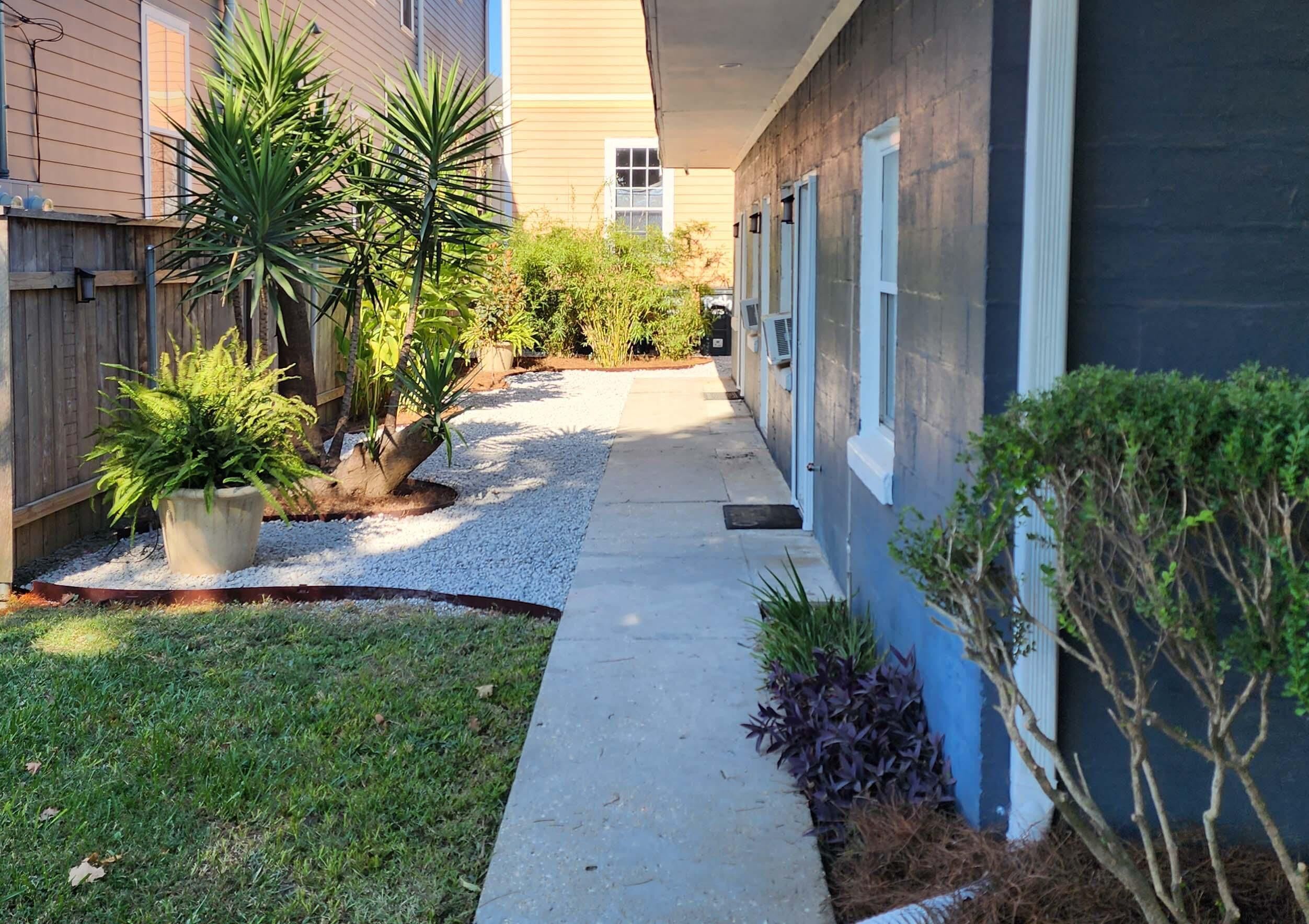 A narrow pathway leading to a building with a blue exterior and a wooden fence on one side.