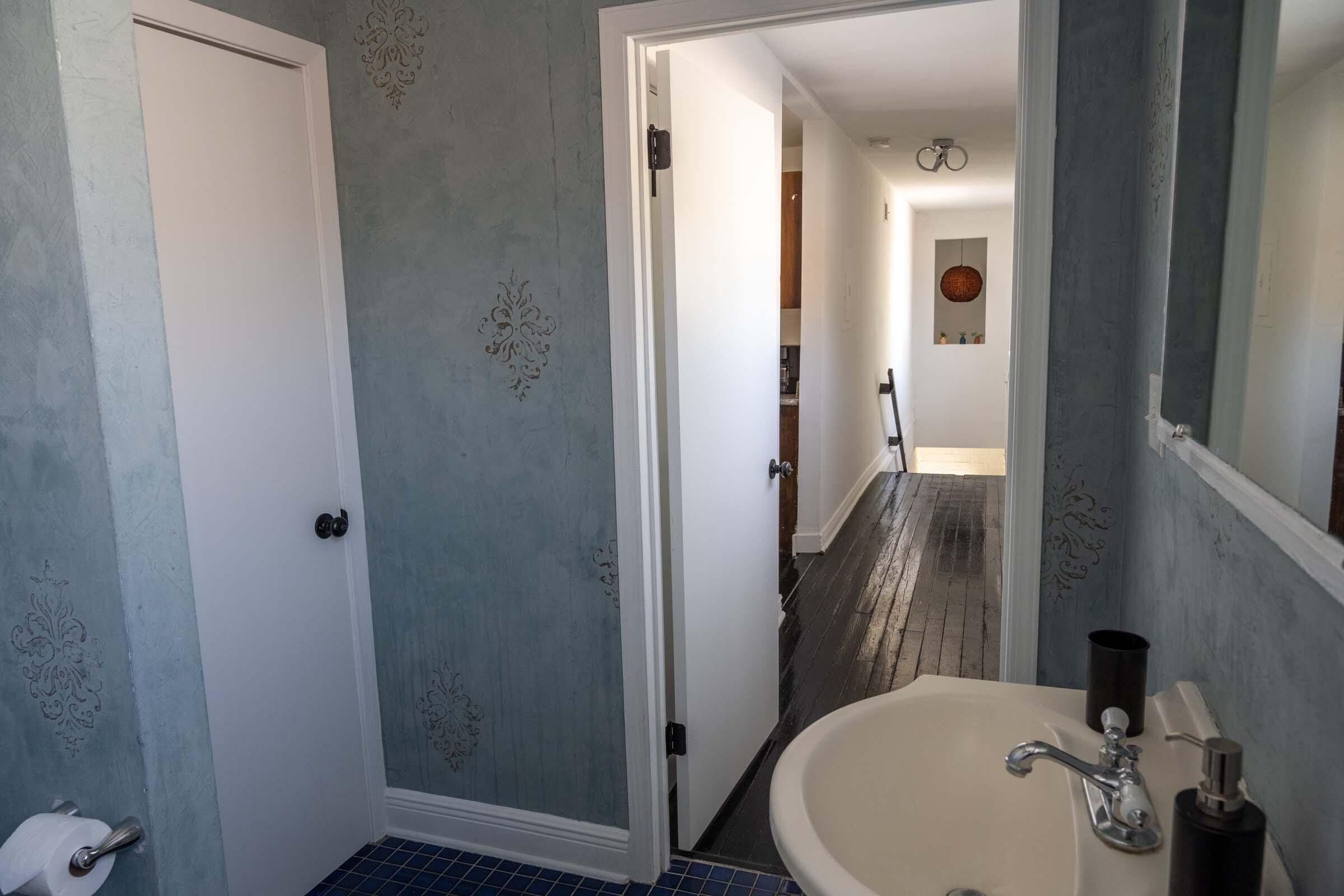 A bathroom with a white sink, a mirror, and a door leading to a hallway.