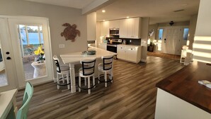 Una cocina moderna con armarios blancos, una isla central y un comedor con cuatro sillas.