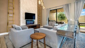 A modern living room with a flat-screen TV, grey sofas, a wooden coffee table, and a glass-top dining table.