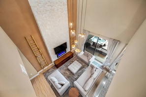 Un soggiorno moderno con una televisione a schermo piatto, una scala in legno e un'ampia finestra con vista su un balcone.