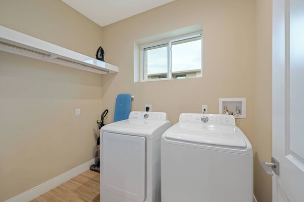 A laundry room with two front-loading washing machines, a window, and a built-in shelf above the machines.