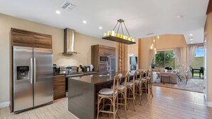 A modern kitchen with a stainless steel refrigerator, a built-in island with bar stools, and a large window offering a view of the outdoors.