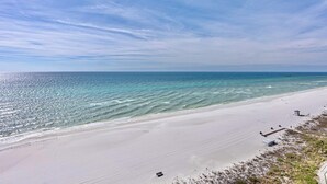 Una platja amb cel serè, mar tranquil·la i un moll a la distància.