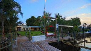 A wooden dock extending into calm water, with a swing chair and a white storage box on the dock. - Cool Breeze. A comfortable house with a tropical backyard waterfront view.  (Naples)