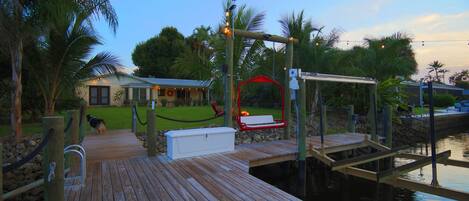 A wooden dock extending into calm water, with a swing chair and a white storage box on the dock.