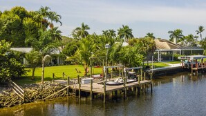 A waterfront property with a dock, a grassy lawn, and a house with a covered patio area. - Cool Breeze. A comfortable house with a tropical backyard waterfront view.  (Naples)