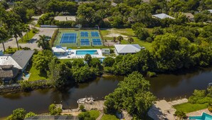 An aerial view of a property with a swimming pool, tennis courts, and a dock. - Cool Breeze. A comfortable house with a tropical backyard waterfront view.  (Naples)