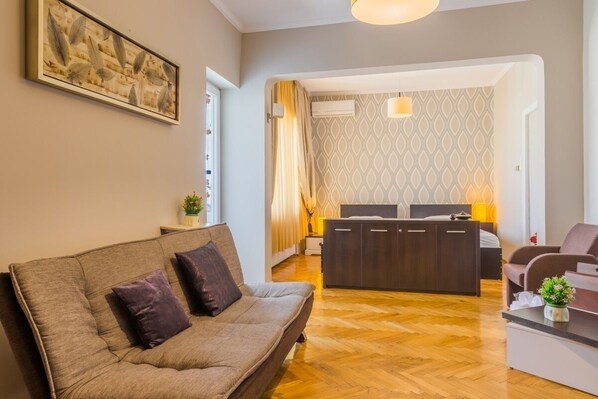 A modern living room with a sofa, a small table, and a desk. There is a patterned wallpaper and a painting on the wall.
