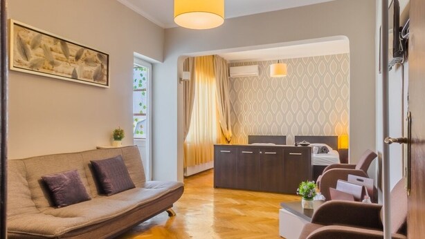 Una sala de estar moderna con un sofá, sillones, una mesa de centro y un comedor, con una cocina al fondo.