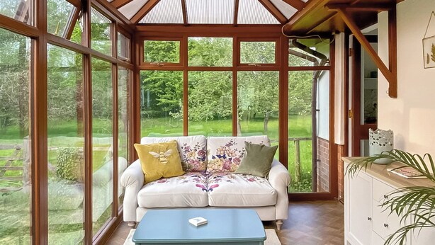 Ein Wintergarten mit einem weißen Sofa, einem blauen Tisch und Blick auf einen grünen Garten.