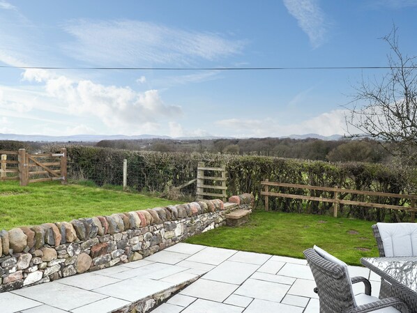 A stone wall, a wooden gate, and a grassy area with a view of distant hills.