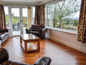 A living room with leather sofas, a glass coffee table, and a view through large windows.