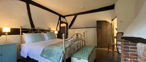 Quarto com uma cama de dossel, um banco de madeira, uma mesa de cabeceira e uma lareira de tijolos.