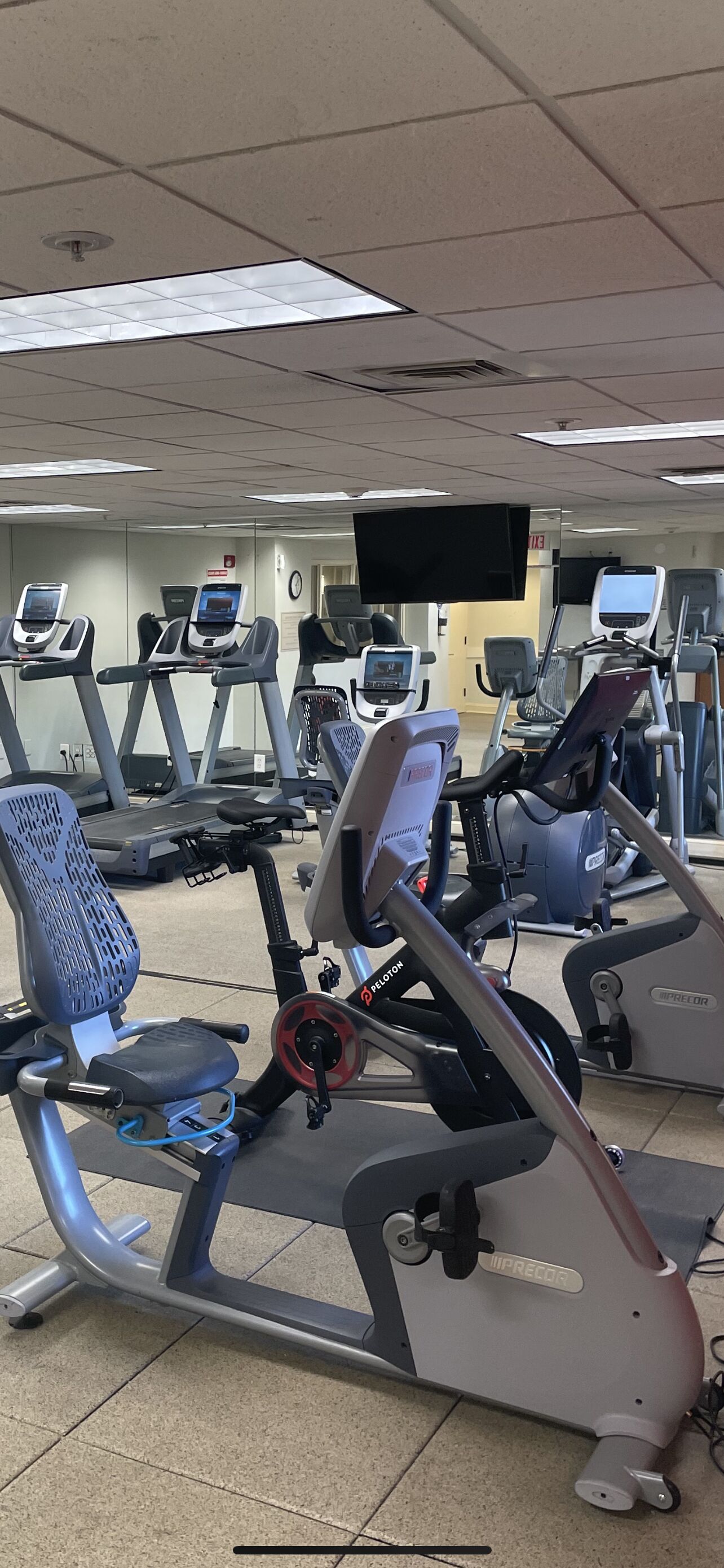Una palestra con diverse macchine per esercizi, tra cui tapis roulant ed ellittiche, disposte in file.
