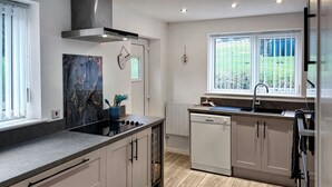A modern kitchen with a built-in dishwasher, a stove, and a window with a view of greenery.