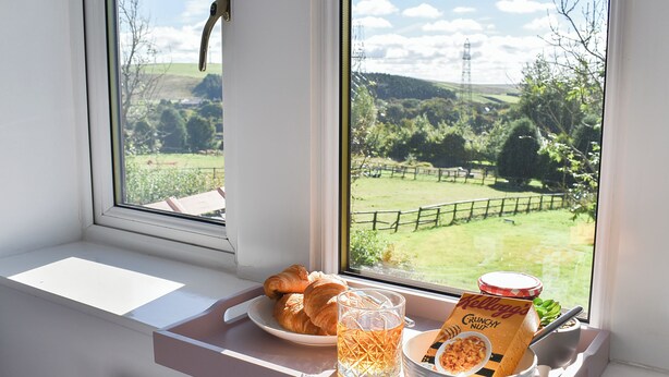 A breakfast tray with croissants, a glass of juice, and a bowl of cereal on a windowsill.