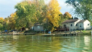 A house by a lake with dock access, surrounded by trees with autumn foliage. - Lakefront Cozy Cabin w/ Dock; 2 BR- 1BA, One Hour from the Twin Cities (Lindstrom)