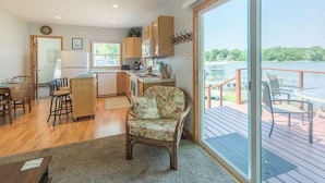 A spacious kitchen with wooden cabinets, a dining area with a table and chairs, and a large sliding glass door leading to a deck with outdoor seating. - Lakefront Cozy Cabin w/ Dock; 2 BR- 1BA, One Hour from the Twin Cities (Lindstrom)