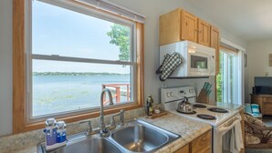 A kitchen with a large window, stainless steel sink, wooden cabinets, and a stove. - Lakefront Cozy Cabin w/ Dock; 2 BR- 1BA, One Hour from the Twin Cities (Lindstrom)