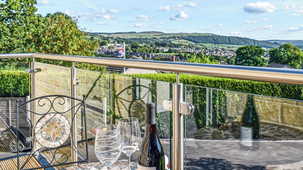 A balcony with a clear view of a village, a flag, and a bottle of wine on a table. - 2 bedroom accommodation in Silsden, near Keighley (Silsden, near Keighley)