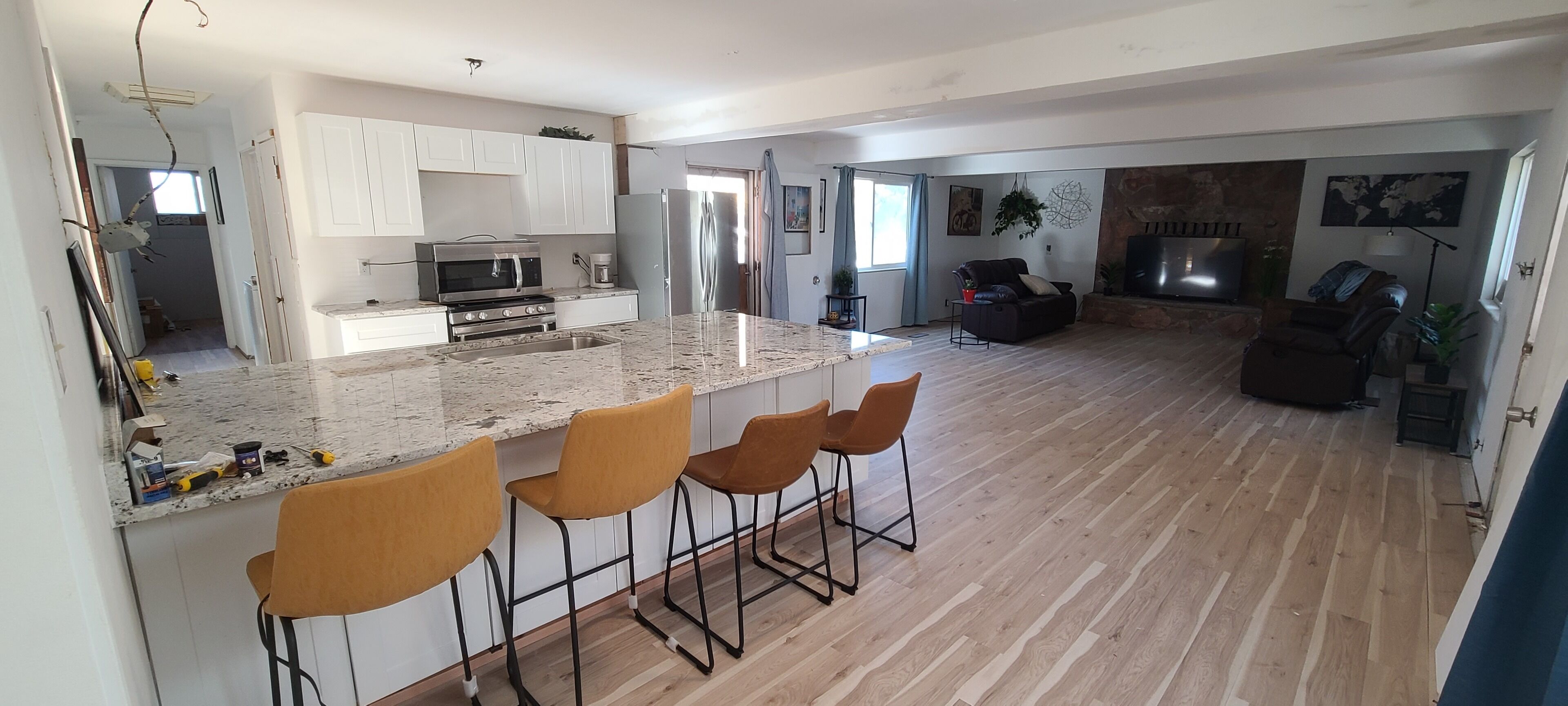 Eine moderne Küche mit Marmorarbeitsplatte, Barhocker und einem Essbereich mit Sofa und Fernseher.