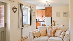A cozy living room with a beige sofa, a small kitchen in the background, and a heart-shaped decoration on the wall.