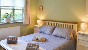 A neatly made bed with a geometric patterned bedspread, two pillows, a tray with tea set, and two towels on the bed.