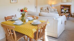 A dining area with a yellow tablecloth, wooden chairs, and a vase of flowers.