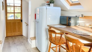 Cocina compacta con refrigerador blanco, sillas de madera, una mesa de comedor y tragaluz.