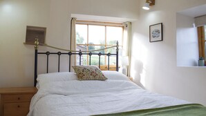 Un dormitorio con una cama, una mesita de noche, una ventana con cortinas, una lámpara de pared y un cuadro enmarcado.