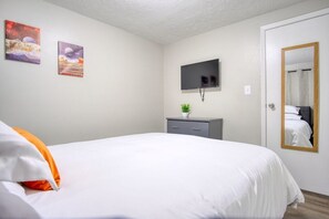 Un dormitorio con cama, televisión, un pequeño armario y dos cuadros en la pared.