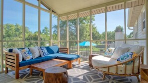 A covered patio with a blue sofa, a wooden table, and a wicker chair. - Modern-Sunroom-15min to DwnTwn-Grps-Kids-Firepit (Indianapolis)