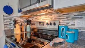 A kitchen with a stainless steel stove, a microwave above it, and a tiled backsplash. There are blue storage containers on the counter. - Modern-Sunroom-15min to DwnTwn-Grps-Kids-Firepit (Indianapolis)