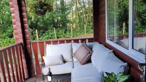 Une terrasse en bois avec un coin salon agrémenté de coussins, une table avec une bouteille et des en-cas, et une plante en pot.